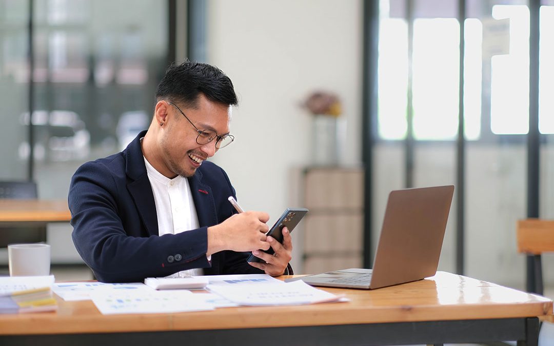 Portrait of a male business owner showing a happy smiling face as he has successfully invested his business using computers and financial budget documents at work.