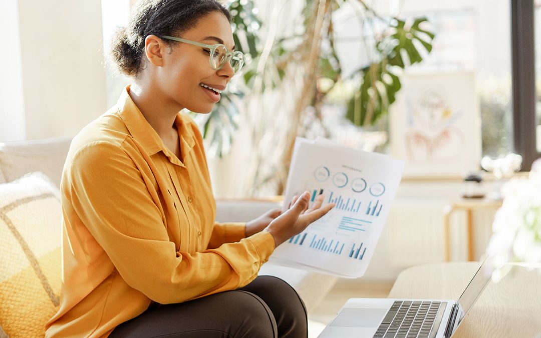 Smiling African American business woman holding documents and talking to laptop